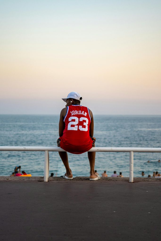 A man in a jersey relaxes by the sea in Nice at sunset, enjoying leisure time.